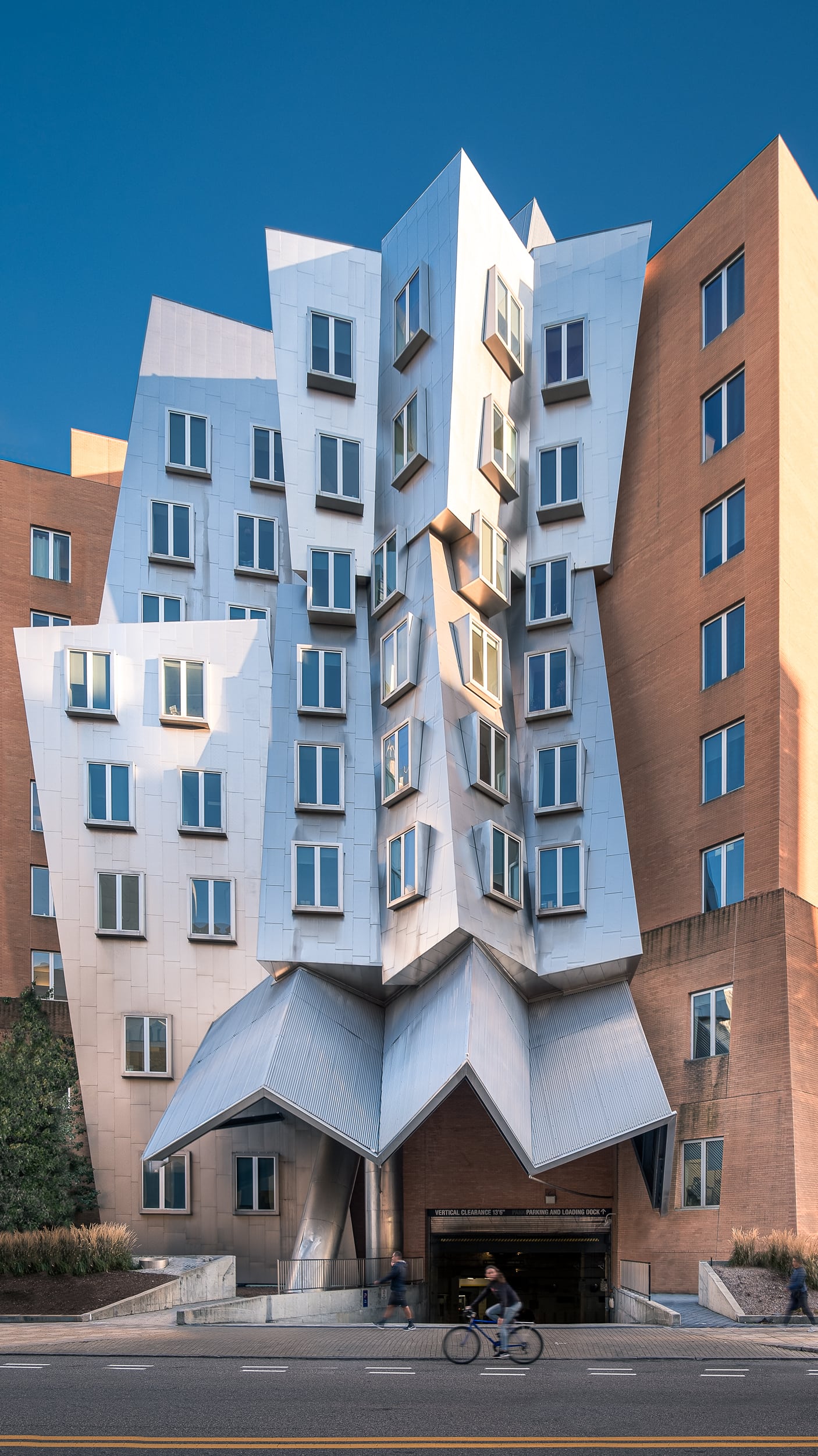 Architectural photography of the Ray and Maria Stata Center at the Massachusetts Institute of Technology (MIT) in Boston designed by Frank Gehry featuring a side angle capturing the brick and aluminum main building in a one point perspective straight on
