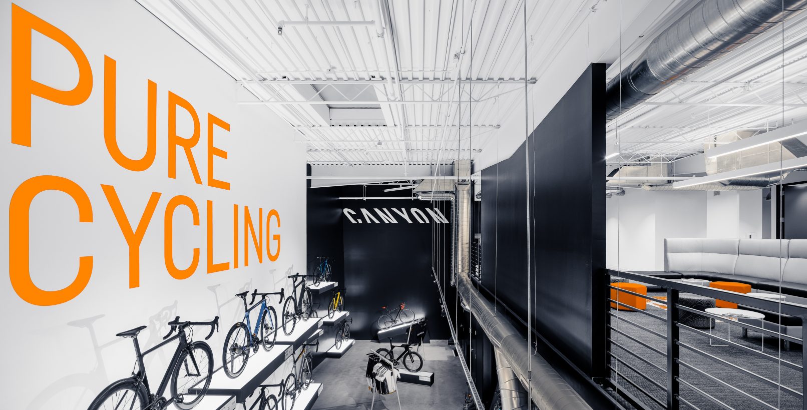 Commercial Interior Design Photography of the Canyon Bicycle Store in Carlsbad California featuring a stark black and white interior with Orange text stating Pure Cycling and White text stating Canyon on the walls and a wall of bicycles displayed on cantilevered shelves on the left and exposed ductwork on the right