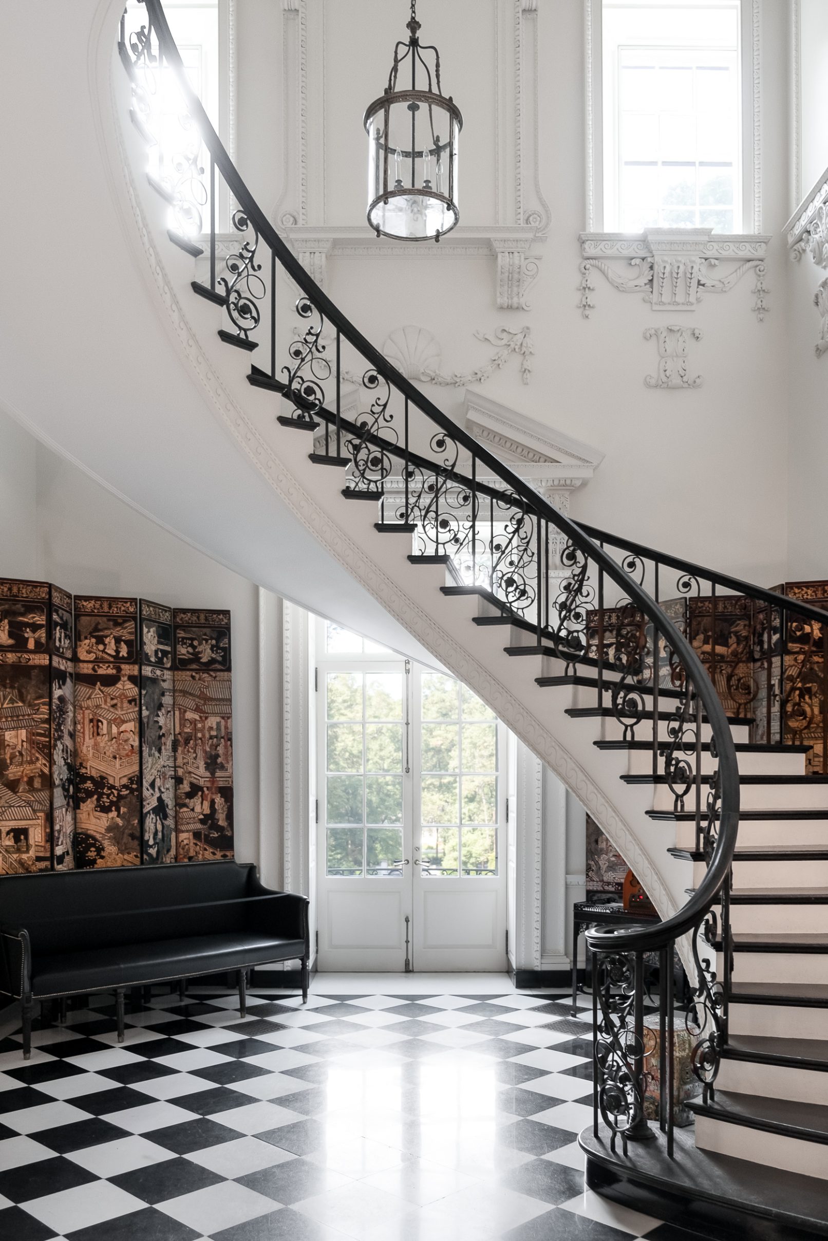 Interior Design Photography of a dramatic staircase in an Orange County California mansion with a black and white checkered floor and bold windows with old world plaster decor surrounding them