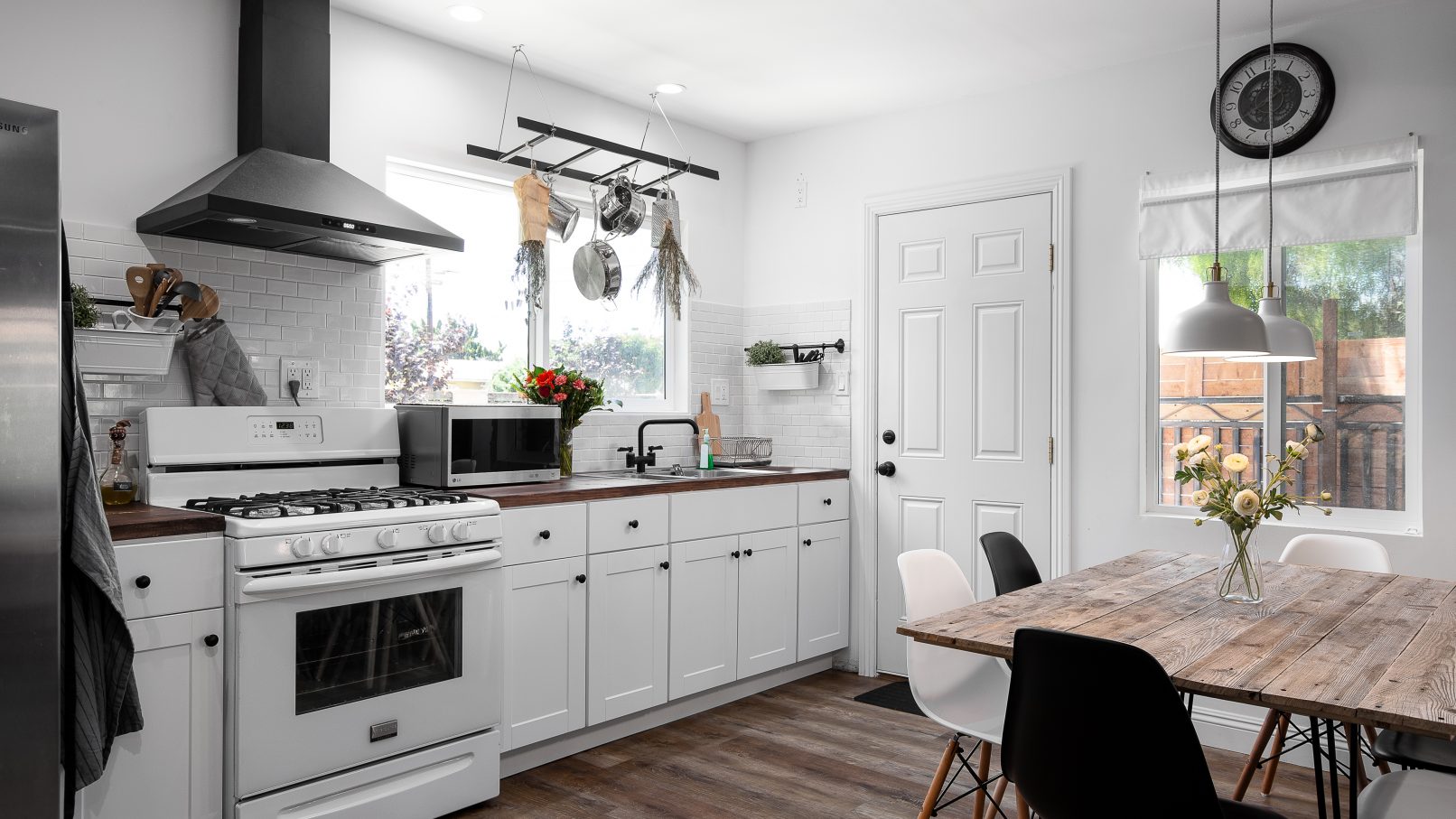 Interior Design Photography in Orange County California of a white kitchen in a modern farmhouse style with Eames chairs around a kitchen table and herbs hanging just above the stainless steel farmhouse sink