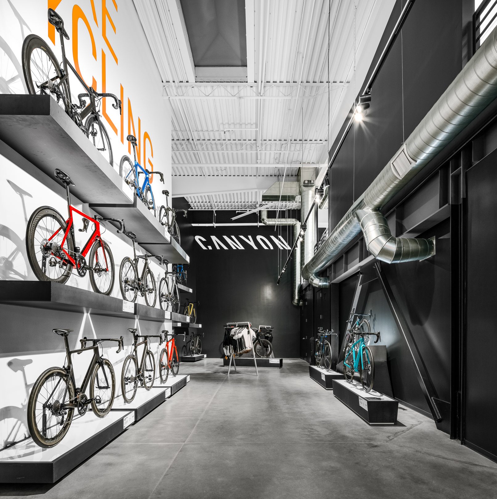 Commercial Interior Design Photography of the Canyon Bicycle Store in Carlsbad California featuring a stark black and white interior with Orange and White text on the walls and a wall of bicycles displayed on cantilevered shelves on the left and exposed ductwork on the right