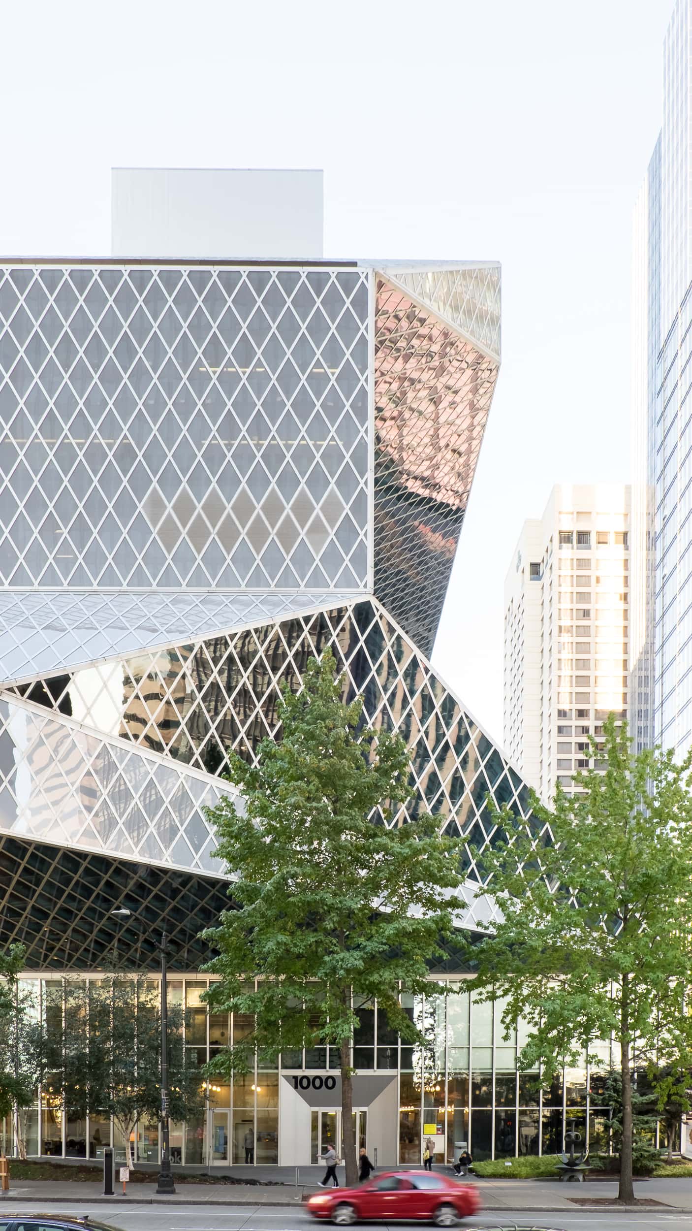 Architectural photography of the Seattle Central Library designed by OMA featuring a one point perspective of the exterior bathed in bright afternoon light as a red car drives past